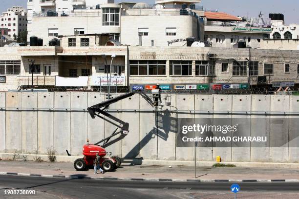 Israeli workers add barbed wire to the top of the wall in the West Bank village of Al-Ram the lies between Jerusalem and Ramallah city on August 6,...