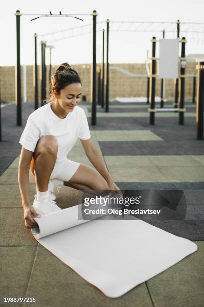 happy smiling woman preparing exercise mat for workout on outdoors sports ground - rolled up yoga mat stock pictures, royalty-free photos & images