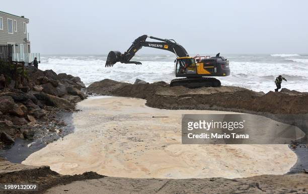 Workers shore up coastline next to homes as a powerful long-duration atmospheric river storm, the second in less than a week, continues to impact...
