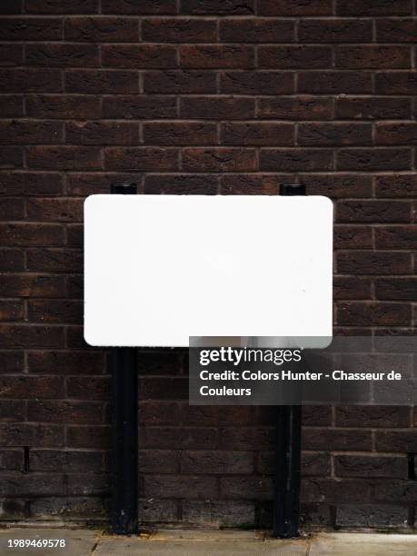 an empty and white street name sign on a sidewalk and in front of a brown brick wall 
in london, england, united kingdom. sunlight. natural colors.
no tag, graffiti or street art. - commercial sign stock illustrations stock pictures, royalty-free photos & images