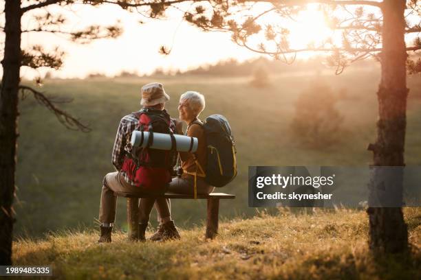 glückliche ältere wanderer, die sich bei sonnenuntergang auf einer bank in der natur unterhalten. - wanderer stock-fotos und bilder