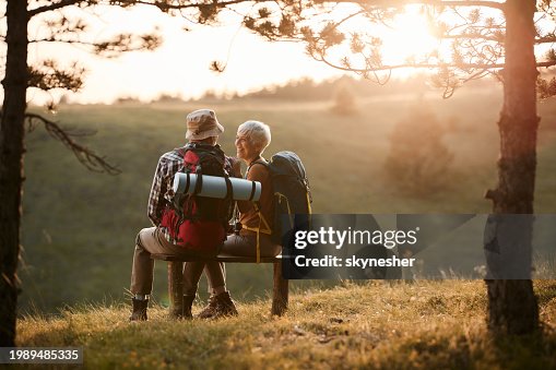 Happy senior hikers talking on a bench in nature at sunset. Happy senior hikers talking on a bench in nature at sunset.
