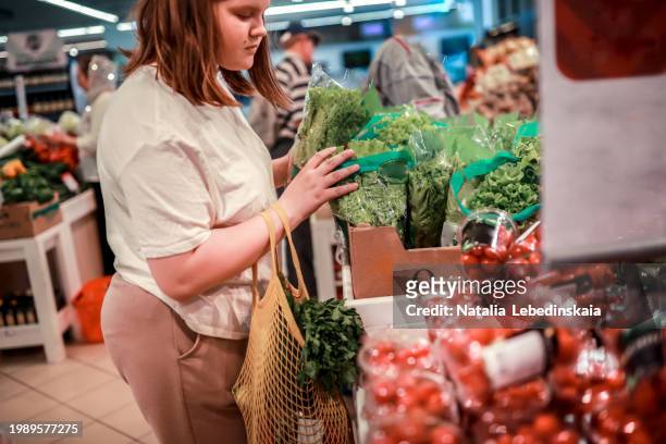 mindful shopping: young plus size woman teenager selecting crisp salad greens using a multi-use mesh bag for health-conscious and sustainable food choices. - fat girls stock-fotos und bilder