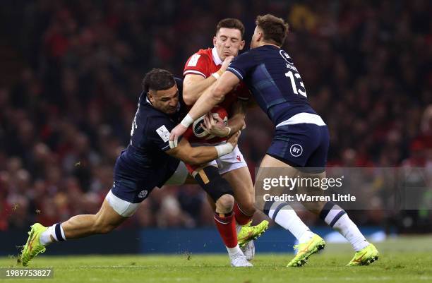 Josh Adams of Wales is tackled by Sione Tuipulotu and Huw Jones of Scotland during the Guinness Six Nations 2024 match between Wales and Scotland at...