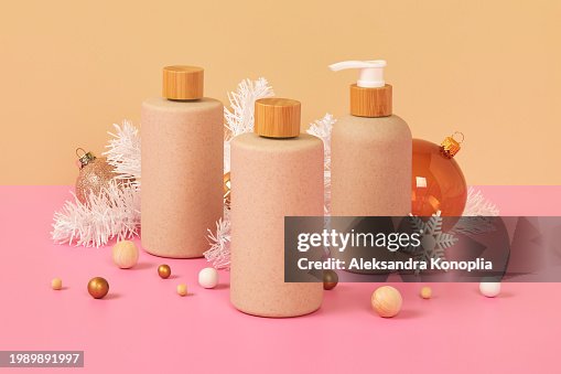 Pastel colored 3D stage with set of organic cosmetics packaging from natural materials on pink table with white Christmas tree and abstract ornaments with cream beige background