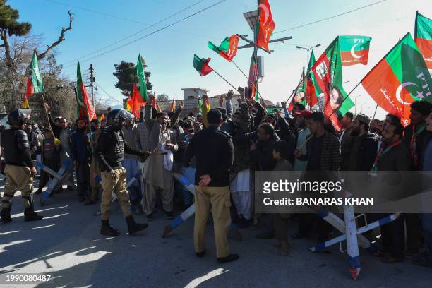 Police personnel stand guard as supporters of Pakistan Tehreek-e-Insaf and other parties protest outside the office of a Returning Officer in Quetta...