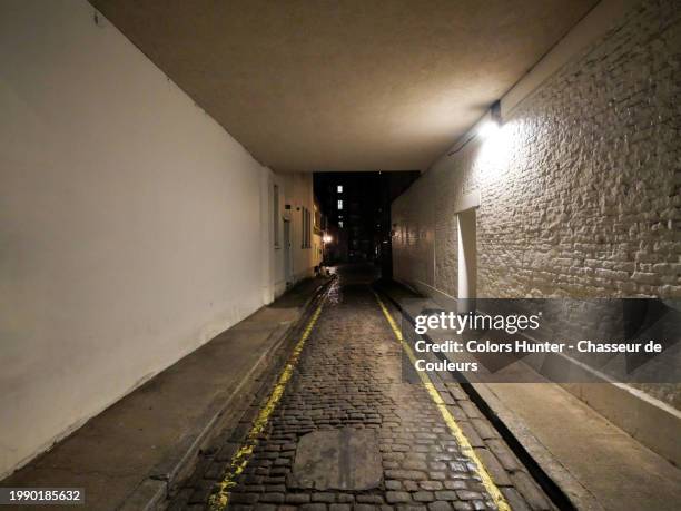 a narrow, cobbled street under a house that gives access to a mews in london, england, united kingdom. night shot. electric light. natural colors. - cobblestone floor stock pictures, royalty-free photos & images