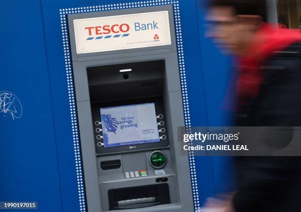 Pedestrian walks past a Tesco Bank cash machine, in central London, on February 9, 2024. British bank Barclays said on February 9, 2024 it had agreed...