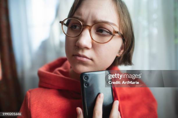 concerned, sad, tired and worried young woman with smartphone at home reading some bad news or having problems - romance fraud stock pictures, royalty-free photos & images