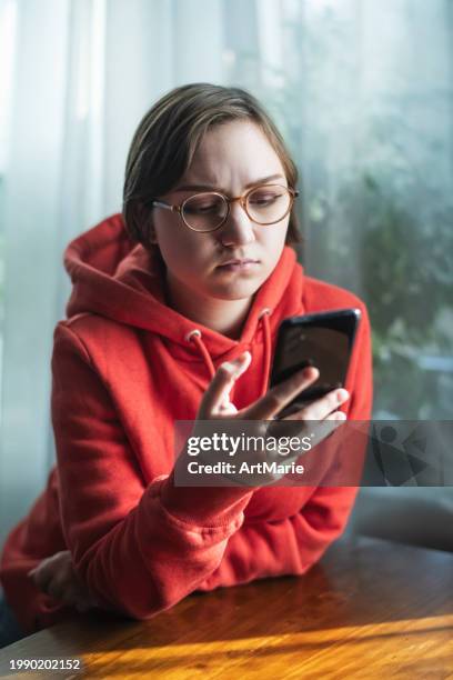concerned, sad, tired and worried young woman with smartphone at home reading some bad news or having problems - scam victim stock pictures, royalty-free photos & images