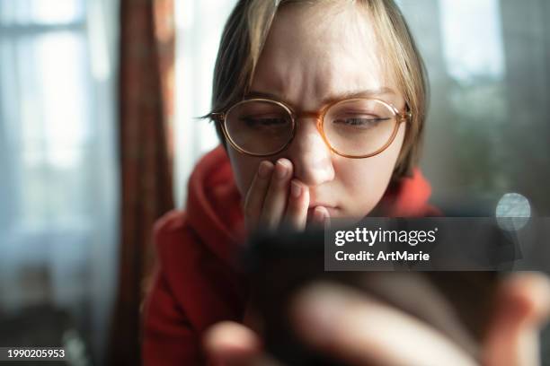 concerned, sad, tired and worried young woman with smartphone at home reading some bad news or having problems or fraud - scam victim stock pictures, royalty-free photos & images