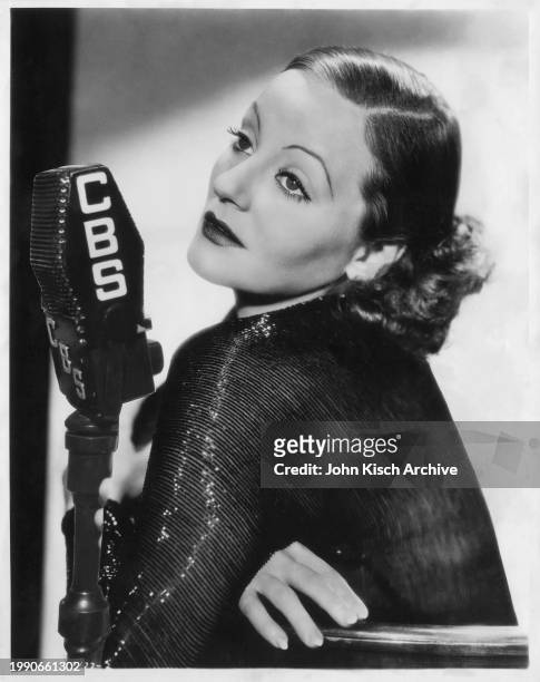 Publicity portrait of American actress Tallulah Bankhead as she poses with a microphone , 1950.