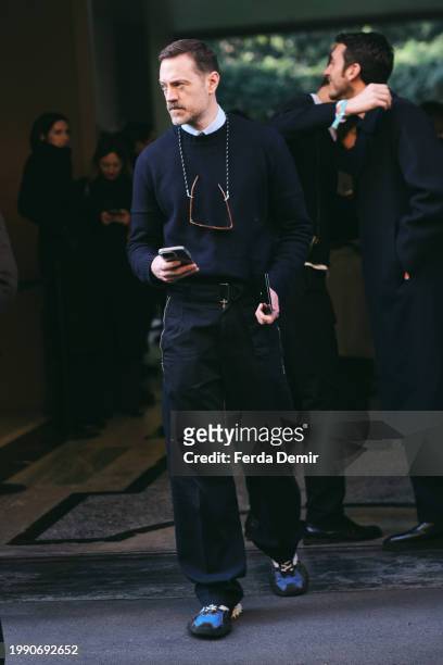 Guest wears navy blue crewneck jumper with black wrinkled gabardine fastener pant outside Giorgio Armani show during the Milan Fashion Week -...
