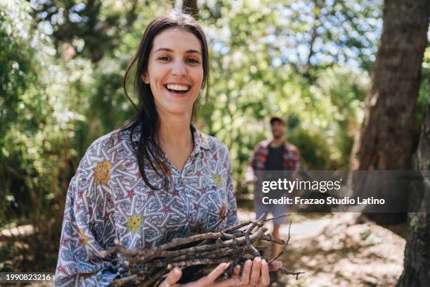 portrait of a young woman carrying firewood for a bonfire while camping in the forest - bonfire stock pictures, royalty-free photos & images