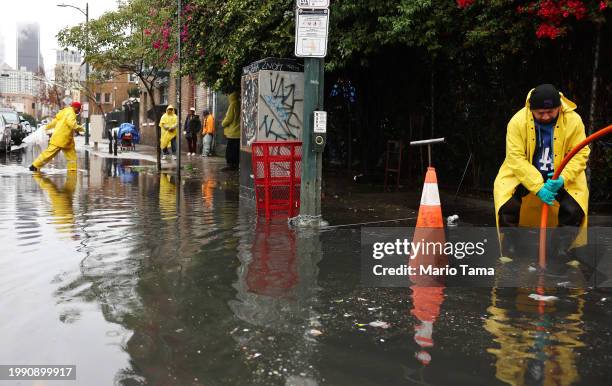 Workers attempt to clear a downtown storm drain as a powerful long-duration atmospheric river storm, the second in less than a week, continues to...