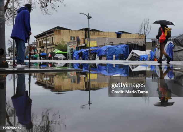 People gather near an encampment of unhoused people in Skid Row as a powerful long-duration atmospheric river storm, the second in less than a week,...