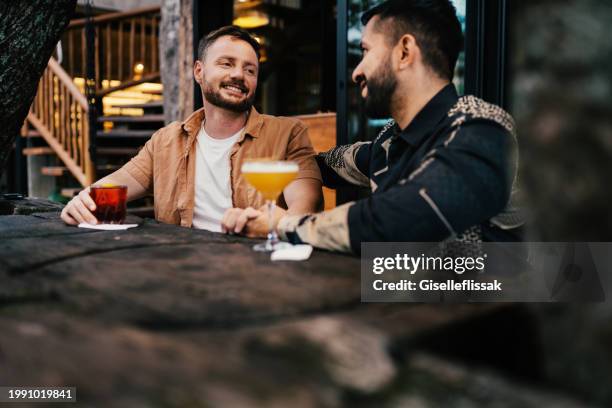 smiling gay couple talking over drinks on a bar patio in the evening - day in the life series stock pictures, royalty-free photos & images