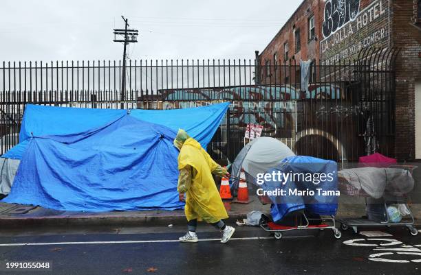 Person walks with carts in the rain near an encampment of unhoused people in Skid Row as a powerful long-duration atmospheric river storm, the second...