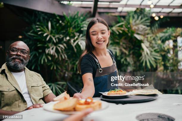 smiling waitress bringing food to a family in a restaurant - empregado de mesa imagens e fotografias de stock