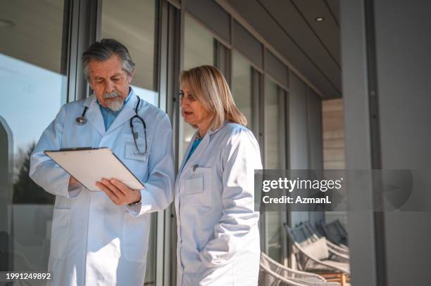 senior caucasian ophthalmologist and mature caucasian female colleague discussing about a patient - urologist stock pictures, royalty-free photos & images