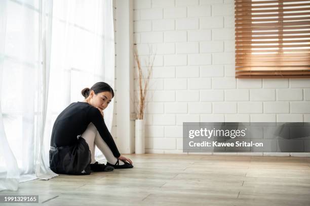 asian upset ballerina sitting on floor after practice dancing ballet. attractive young woman ballet dancer in tutu and pointe shoes, feel pain and tired, massaging or stretching her foot in dance hall - ballet feet hurt stock pictures, royalty-free photos & images