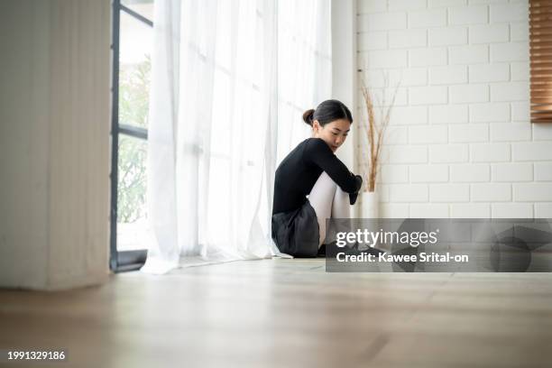 asian upset ballerina sitting on floor after practice dancing ballet. attractive young woman ballet dancer in tutu and pointe shoes, feel pain and tired, massaging or stretching her foot in dance hall - ballet feet hurt stock pictures, royalty-free photos & images