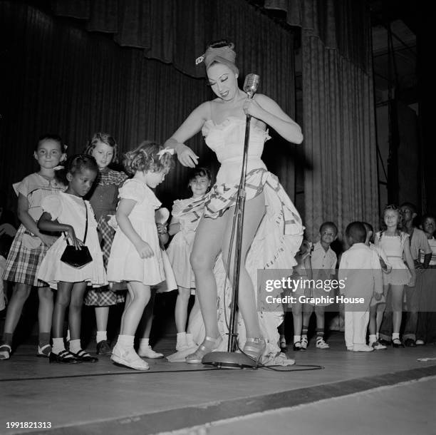 American-born French singer, dancer and actress Josephine Baker, wearing a high-low skirt and a headscarf, on stage with a group of children, during...