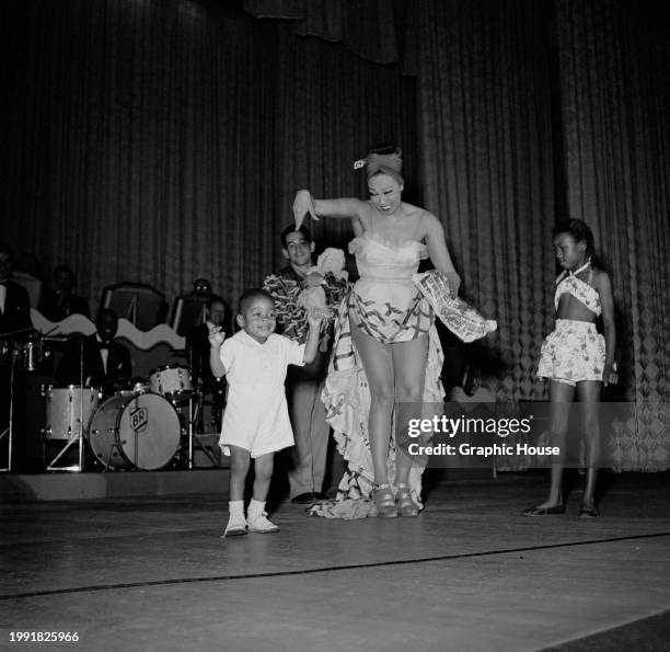 American-born French singer, dancer and actress Josephine Baker, wearing a high-low skirt and a headscarf, on stage with a group of children, during...