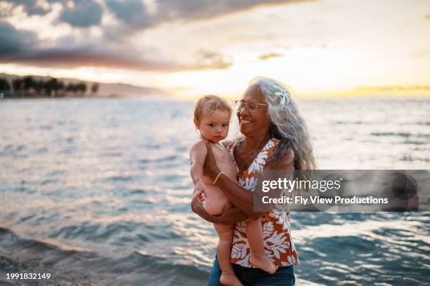 vibrant woman walks on the beach holding grandson - pacific islanders stock pictures, royalty-free photos & images