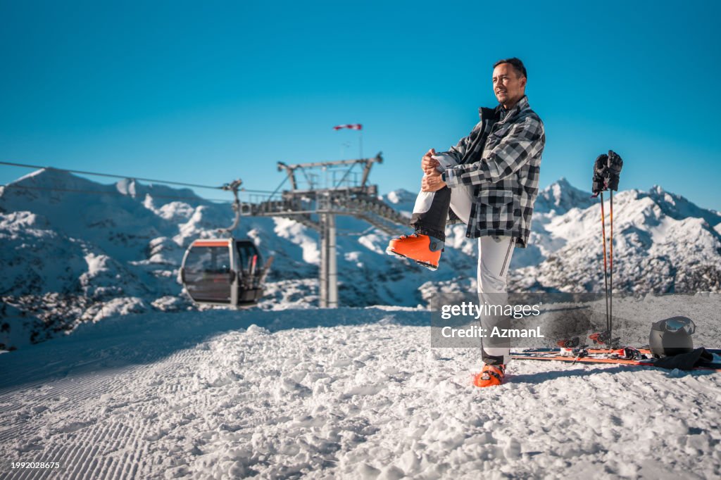 Mid Adult Asian Male Preparing for Skiing on Snowy Mountain