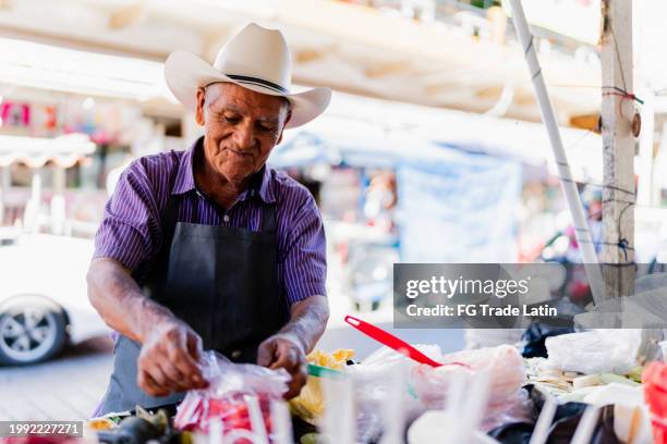 senior man selling fruit to customer at market stall - cowboy hat shop stock pictures, royalty-free photos & images