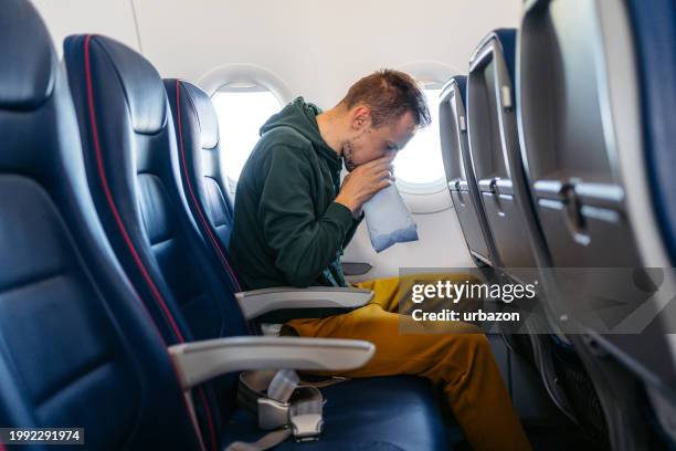 junger mann übergibt sich in einem krankensack in einem flugzeug - brechreiz stock-fotos und bilder