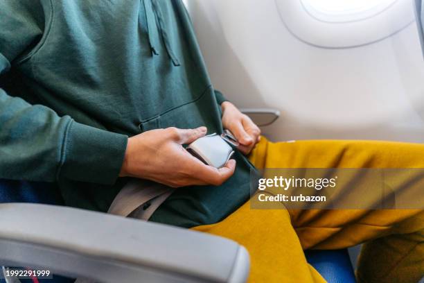 young man fastening his seatbelt in an airplane - fastening stock-fotos und bilder