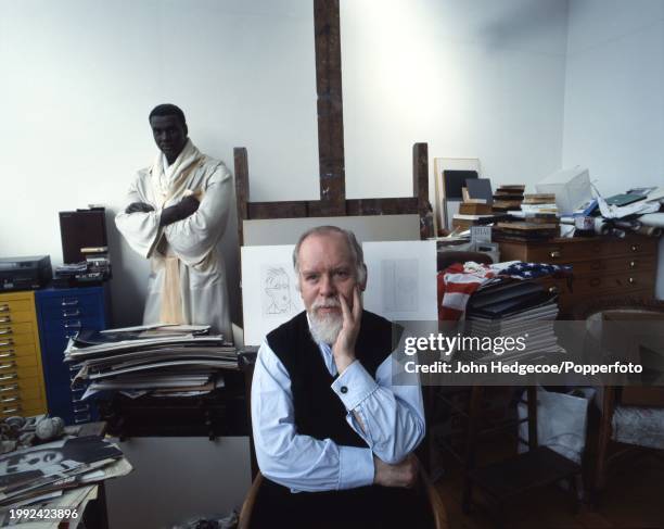 English artist Peter Blake seated on a chair in front of an easel at his home studio workplace in London in 1992. Visible behind Blake is a wax...