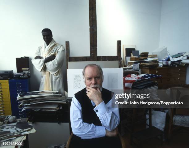 English artist Peter Blake seated on a chair in front of an easel at his home studio workplace in London in 1992. Visible behind Blake is a wax...