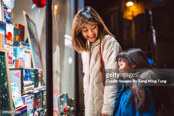 mom & daughter looking at the window display of a gift shop at night - value for money stock pictures, royalty-free photos & images