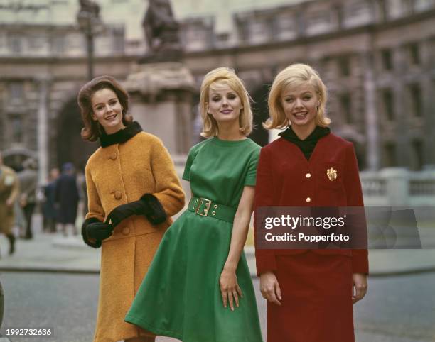 Three female fashion models posed wearing, from left, an orange princess coat with fur collar, a green belted dress and a red corduroy casual jacket...