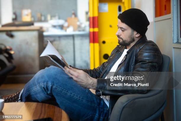 joven sentado despreocupado leyendo una revista - biker lifestyle magazine fotografías e imágenes de stock