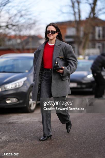 Guest wears sunglasses, earrings, a white t-shirt, a red pullover, a gray oversized blazer jacket , a black leather bag, gray denim jeans pants,...