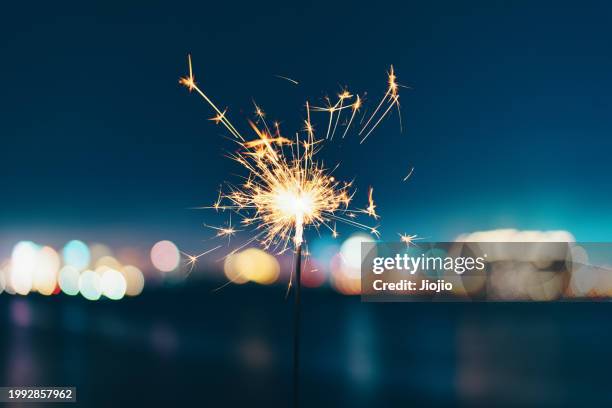 burning sparkler against sky - brilhante fogo de artifício imagens e fotografias de stock
