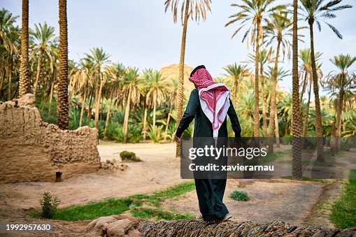 Saudi man walking through date palm grove, Al-Ula