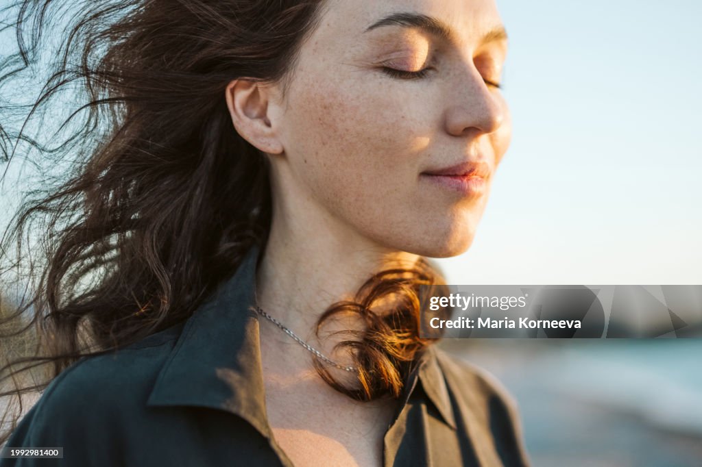 Portrait of a calm woman with hair flying in the wind on the beach.