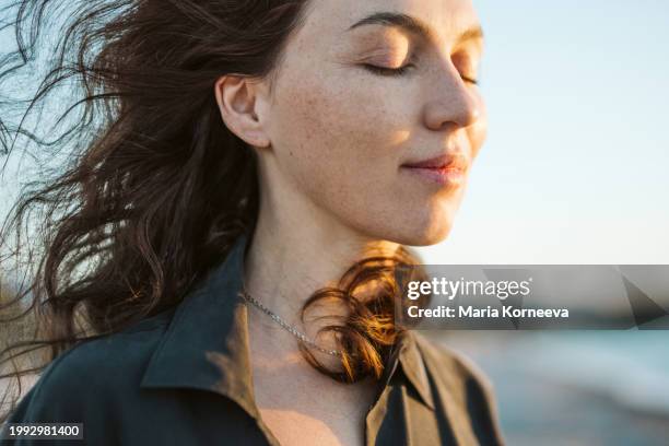 portrait of a calm woman with hair flying in the wind on the beach. - calm before the storm stock pictures, royalty-free photos & images
