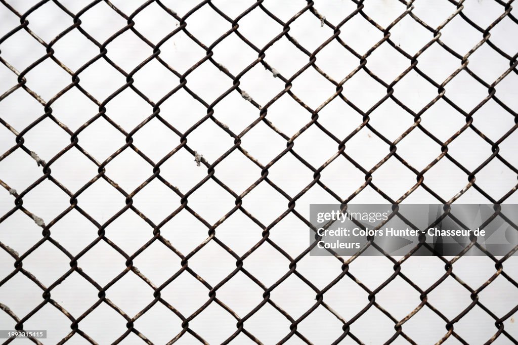 Close-up of a weathered metal fence with a white wall in the background. Sunlight. Natural colors. Montreal, Quebec, Canada.