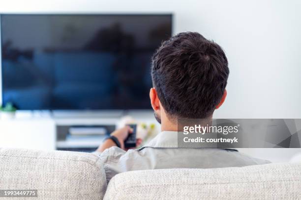 man watching tv on the sofa during the day. - smart tv living room stock pictures, royalty-free photos & images
