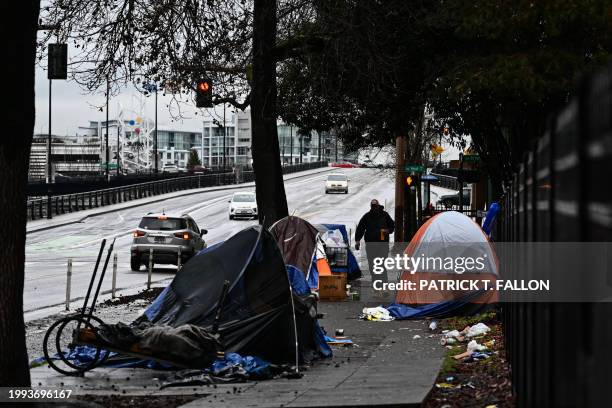 Pedestrian walks past an encampment of tents after crossing Hoyt Street in Portland, Oregon on January 24, 2024. In the midst of a presidential...