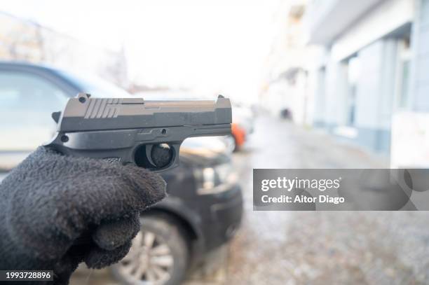 a person holds a gun ready to shoot in a street. - disparar fotografías e imágenes de stock