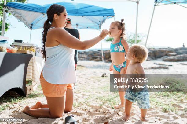 woman sharing a bite of food with her niece while barbecuing at the beach - nephew stock pictures, royalty-free photos & images