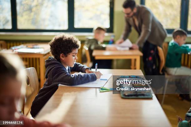 schwarzer schüler, der in einer grundschulklasse schreibt. - schulbedarf stock-fotos und bilder