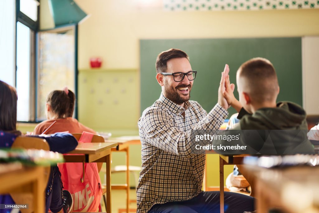 Happy teacher and schoolboy giving each other high-five on a class.